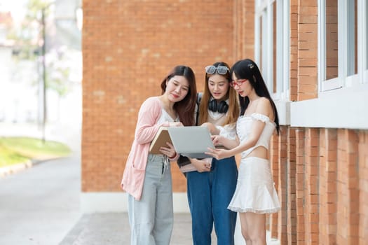 A group of female female students at an Asian university stood outside the classroom talking about their classes on laptops during break time..