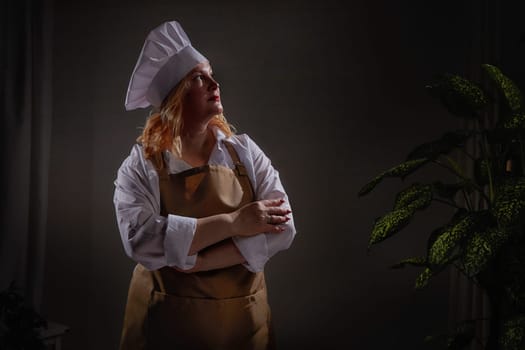 A fat funny female cook in a hat and apron poses in the kitchen and takes selfie. Good cooking and body positive