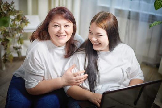 Fat funny funny adult mother and daughter with laptop indoors. A teenage girl teaches a middle-aged woman modern technology. Internet, chatting