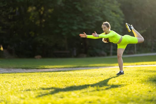 A woman is doing a yoga pose on a grassy field. The grass is green and the sky is blue