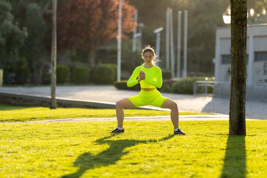 A woman in a neon yellow outfit is doing a yoga pose in a park. Concept of energy and positivity, as the woman is focused on her workout and enjoying the outdoors