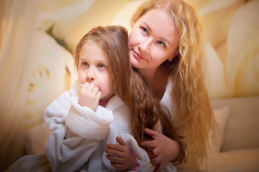 Mother and daughter happily relax and fun together on bed in bedroom. The concept of tenderness between mom and girl