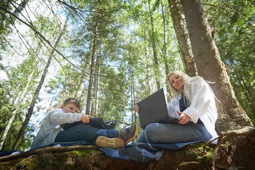 Mother and son with a laptops in the forest in summer. Fat young smart teenage boy and woman working with modern IT technologies in nature