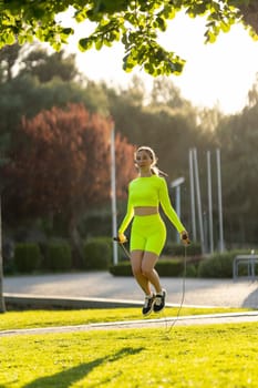 A woman in a neon yellow outfit is jumping rope in a park. Concept of energy and enthusiasm, as the woman is engaged in an active and healthy activity. The bright colors of her outfit