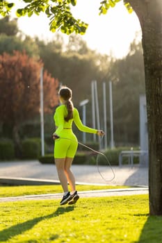 A woman in a neon green outfit is jumping rope in a park. The scene is bright and cheerful, with the sun shining down on the grass and the woman's outfit adding a pop of color to the scene