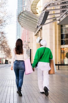 rear view of a multiracial couple of female friends walking in a shopping area, friendship and modern lifestyle concept