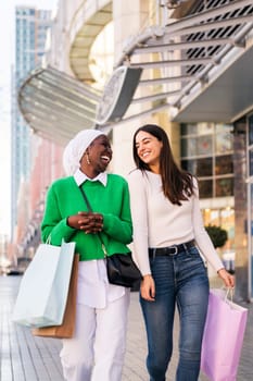 multiracial couple of female friends having fun walking in a shopping area, friendship and modern lifestyle concept