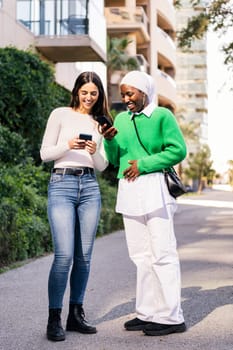 two young women walking down a street looking their cell phones, concept of friendship and technology