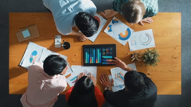 Top down aerial view of smart business people analyze data together at meeting. Group of business team working together and looking at financial chart at tablet placed on meeting table. Convocation.