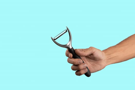 Black male hand holding a potato peeler isolated on cyan background. High quality photo