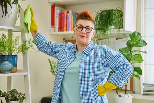 Middle-aged woman cleaning house, female looking at camera, wiping dust in room. Housekeeping, housework, housecleaning, cleaning concept