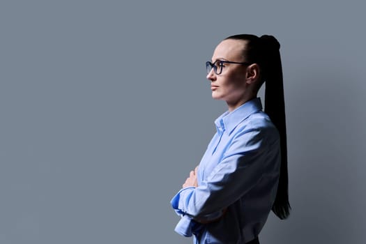 Profile view of middle aged serious woman looking forward, gray studio background, copy space for advertising image text. 30s business confident successful female. Marketing sales services, people