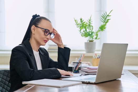 Business woman working in home office at desk with laptop computer. Serious 30s female typing and looking at monitor. Remote business, technologies internet, teaching, blogging, work freelance concept