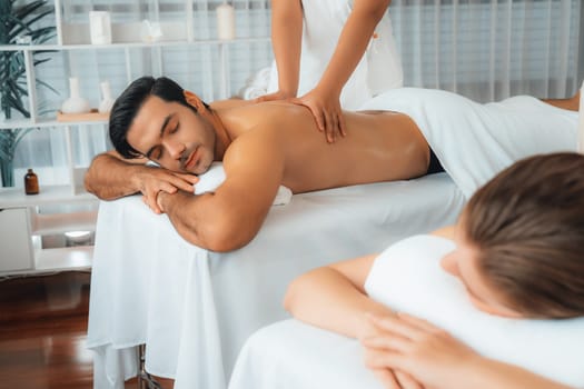 Caucasian couple customer enjoying relaxing anti-stress spa massage and pampering with beauty skin recreation leisure in day light ambient salon spa at luxury resort or hotel. Quiescent