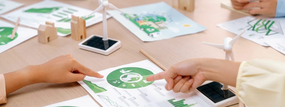 A cropped picture of green city poster was placed at green business meeting on meeting table with environmental document, wooden house block and windmill model scattered around. Closeup. Delineation.