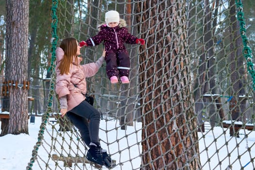 a large public green area in a town, used for recreation.Cheerful mother with a child on a playing net stretched on trees in winter park.