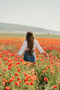 Woman poppies field. Back view of a happy woman with long hair in a poppy field and enjoying the beauty of nature in a warm summer day