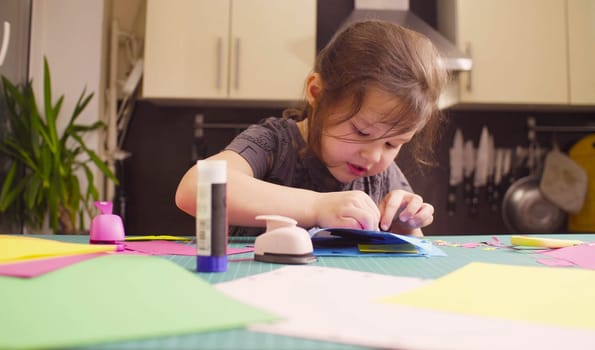 Scrapbooking. Little girl doing a postcard. She is glueing colored paper. Children's creativity, handicraft
