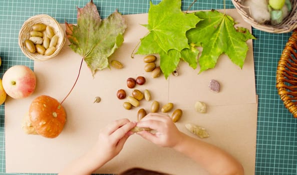 Top view. Autumn. Little girl sitting at the desk makes necklace of acorns and colored balls