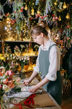 A woman in her florist shop collects bouquets of flowers. The concept of a small business. Bouquets of tulips for the holiday on March 8