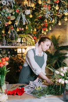 A woman in her florist shop collects bouquets of flowers. The concept of a small business. Bouquets of tulips for the holiday on March 8