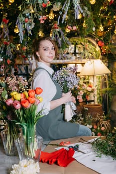 A woman in her florist shop collects bouquets of flowers. The concept of a small business. Bouquets of tulips for the holiday on March 8