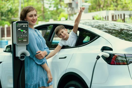 Environmental awareness family with eco-friendly electric car recharging battery from home EV charging station with little boy inside the car. Rechargeable and EV car technology. Perpetual