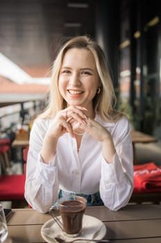 Gen z blonde woman drinks hot chocolate in summer cafe. Tasty beverage and break