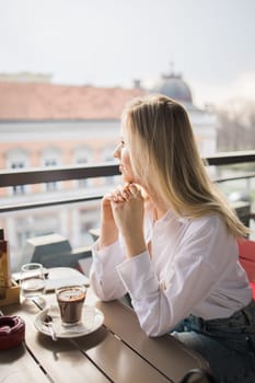 Gen z blonde woman drinks hot chocolate in summer cafe. Tasty beverage and break