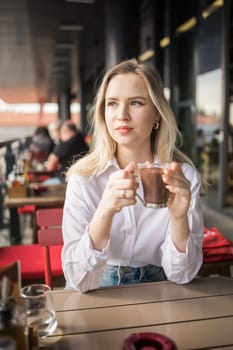 Gen z blonde woman drinks hot chocolate in summer cafe. Tasty beverage and break