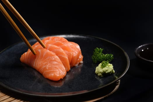 Fresh salmon sashimi on black plate with wasabi and parsley leaf. Japanese food style.