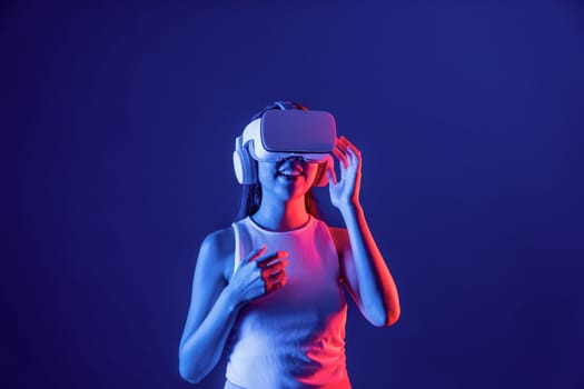 Smart female stand in cyberpunk neon light wearing VR headset connecting metaverse, futuristic cyberspace community technology. Elegant woman excited seeing generated virtual scenery. Hallucination.