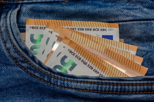 Three folded 50 Euro banknote bills stuck in front pocket of blue jeans 1