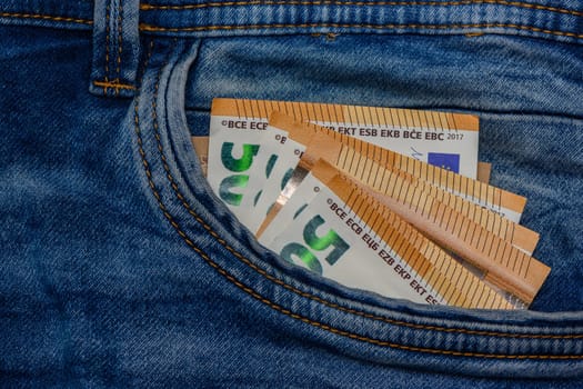 Three folded 50 Euro banknote bills stuck in front pocket of blue jeans