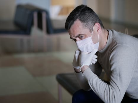 Man wearing protective gloves on hands and mask on face nervously impatiently waiting in the lobby in covid 19 virus