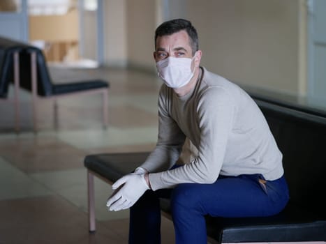 Man wearing protective gloves on hands and mask on face nervously impatiently waiting in the lobby in covid 19 virus