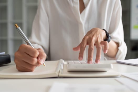 Businesswoman using a calculator to calculate numbers on a company's financial documents, she is analyzing historical financial data to plan how to grow the company. Financial concept.