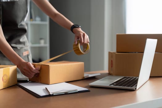 Young business entrepreneur sealing a box with tape. Preparing for shipping, Packing, online selling, e-commerce concept.