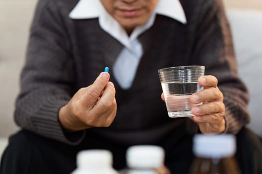 A man is holding a pill and a glass of water. He is sitting on a couch. The man seems to be taking a medication or supplement