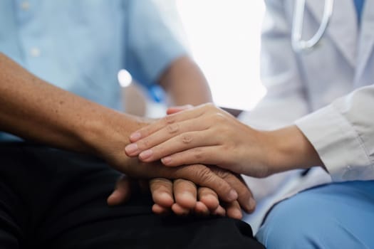 A doctor and a patient are holding hands. The doctor is wearing a white coat