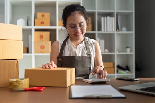 A woman is sitting at a desk with a calculator and a stack of boxes. She is smiling and she is happy