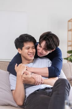 Happy Asian homosexual couple embrace on sofa in living room.