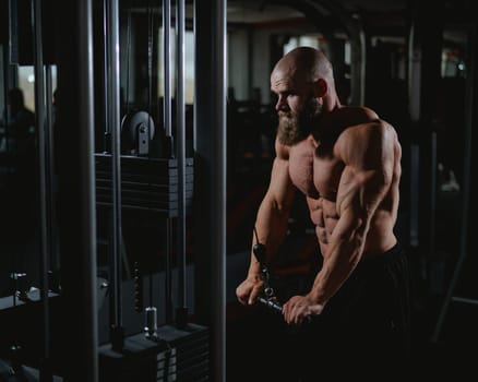Bald Caucasian Bodybuilder doing heavy triceps exercises with cable
