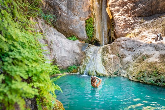 Young happy woman swimming in turquoise blue crystal clear water in the river with a waterfall summer vacation relaxing body and mind. High quality photo