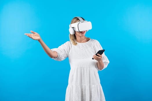 Caucasian girl wearing VR glasses while holding phone and pointing at view. Happy woman surprised while looking around to explore visual reality world or metaverse. Technology innovation. Contraption.