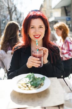 Beautiful happy woman with long red hair enjoying cocktail in a street cafe.
