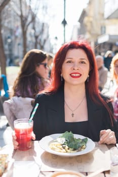 Beautiful happy woman with long red hair enjoying pasta in a street cafe