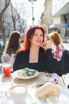 Millennial woman eating italian pasta at restaurant on the street in spring. Concept of Italian gastronomy and travel. Stylish woman with red hair.