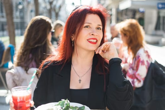 Beautiful happy woman with long red hair enjoying pasta in a street cafe