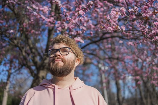 Man allergic enjoying after treatment from seasonal allergy at spring. Portrait of happy bearded man smiling in front of blossom tree at springtime. Spring blooming and allergy concept. Copy space.